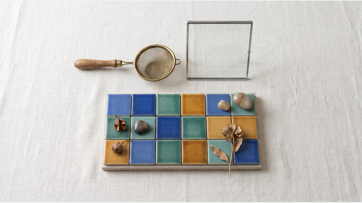 A brass sieve and glass frame inspect the same array of colour-coded tiles without altering it.
