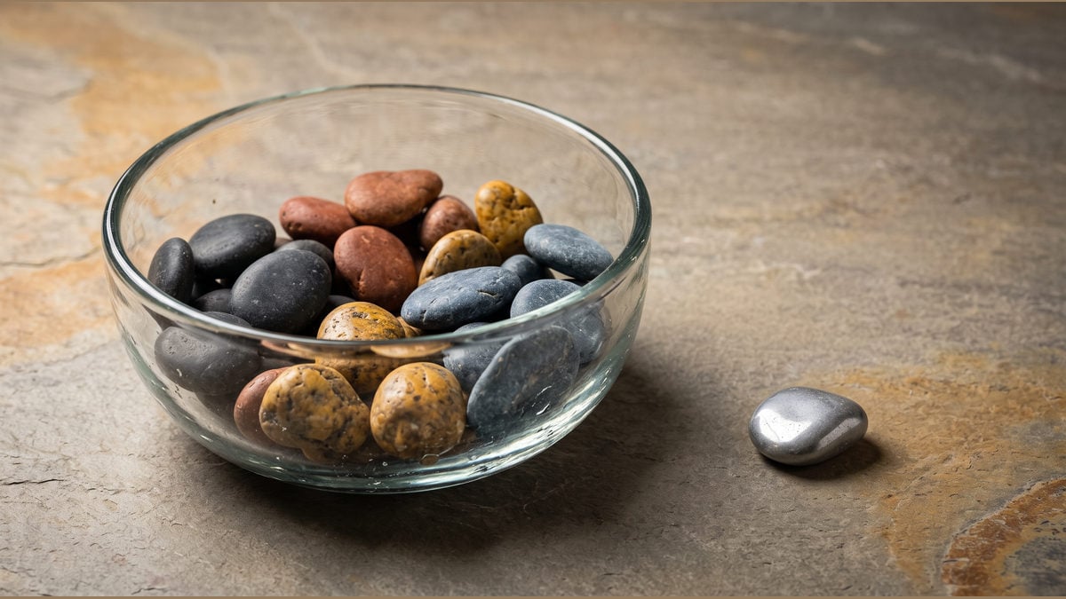 Coloured stones fill a glass bowl while one stone rests separately.