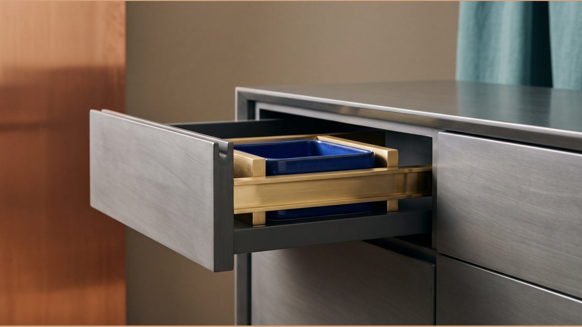 An open grey drawer holds a blue ceramic module within brass rails.