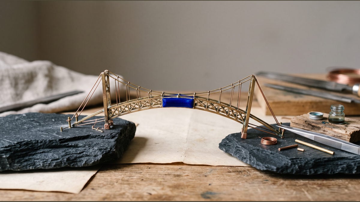 A miniature brass bridge spans two dark stones with a blue segment at its centre.