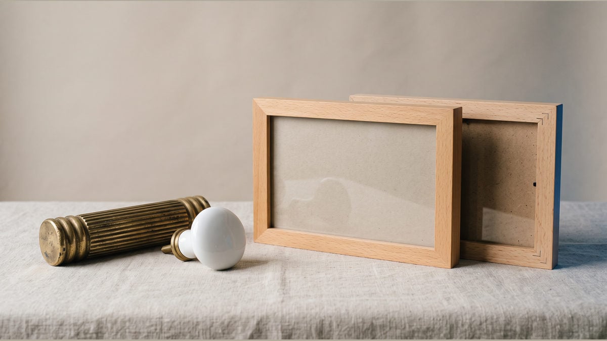 A ribbed brass handle and a white porcelain pull lie beside wooden frames.