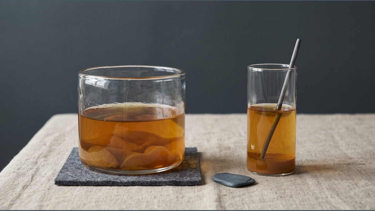 A wide glass vessel and a narrow cup hold amber-coloured material on a pale work surface.