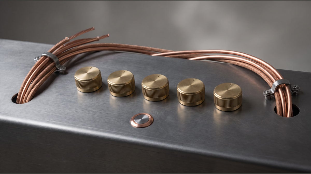 Five blank brass adjustment dials and a recessed button on a brushed-metal bench.