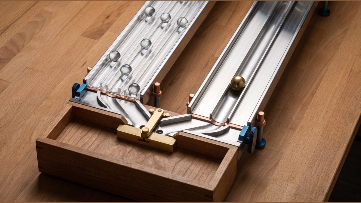 Glass balls in separate steel channels beside one narrow brass-controlled channel.