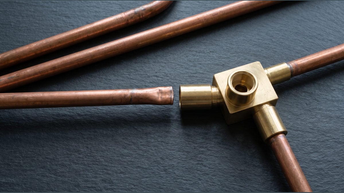 Copper pipes and a brass manifold with one pipe disconnected from its socket.