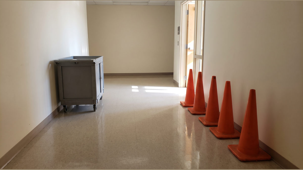 A plain utility cart and aligned safety cones in an empty sunlit corridor.